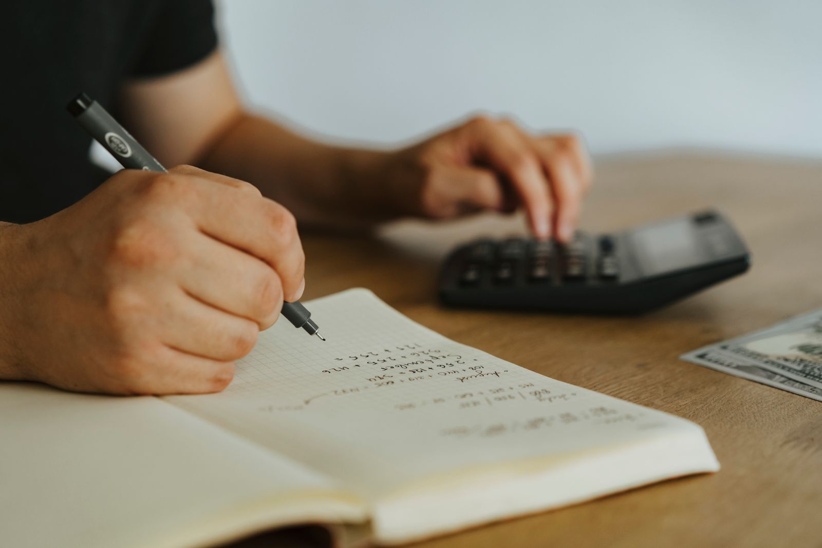 方眼ノートにペンで数字を書き込みながら、もう片方の手で電卓を打っている手元