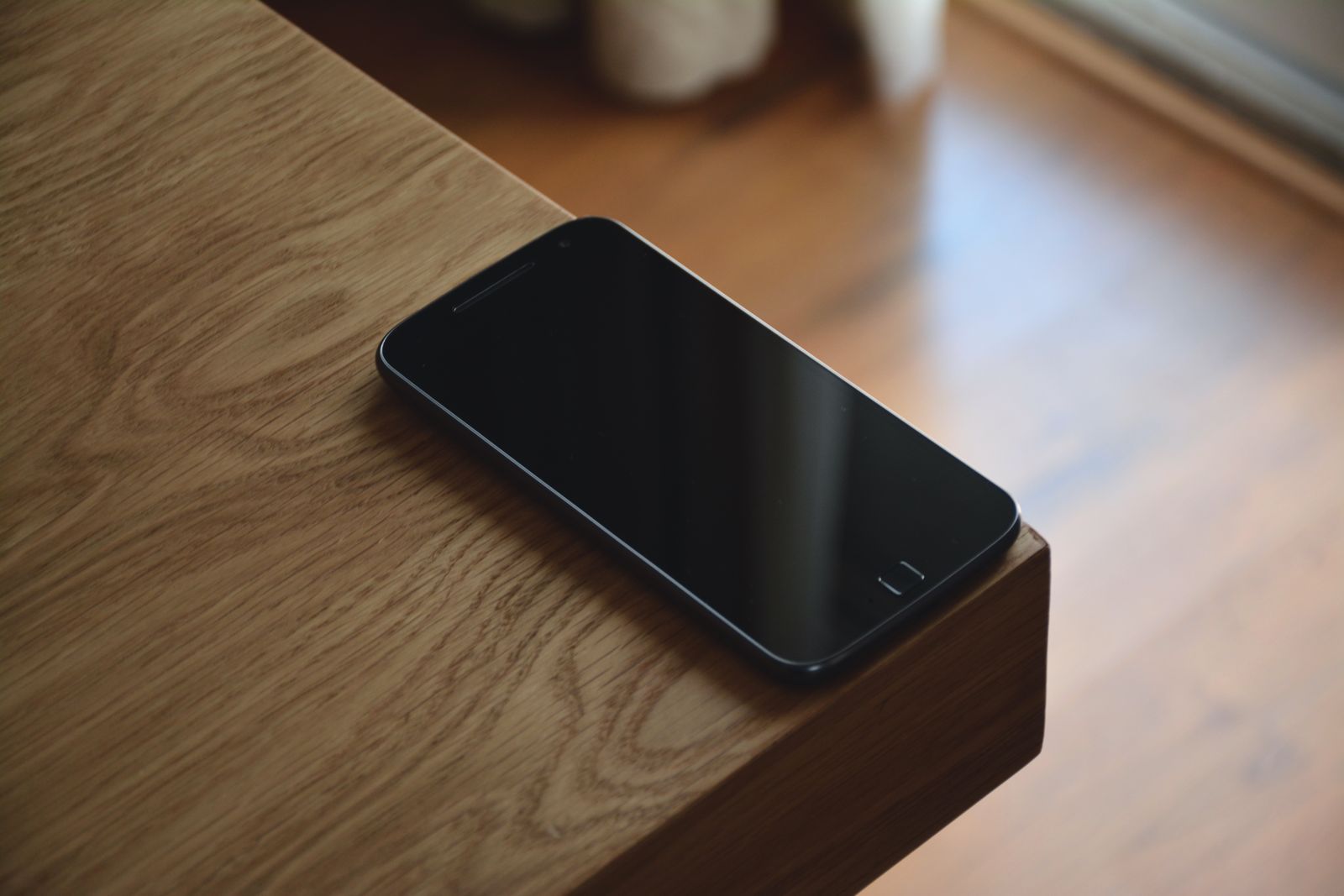木のテーブルの角に、画面を上にして置いた黒いスマートフォン。画面には何も映っていない